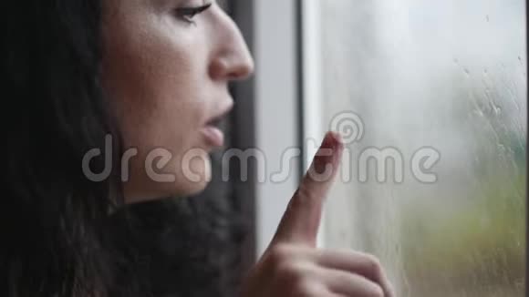 年轻的女人在一扇雾蒙蒙的窗户上画了一颗心微笑着窗外的街道上下雨视频的预览图