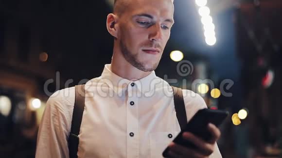 微笑的人在夜间城市使用智能手机一个英俊的年轻人晚上用智能手机喝冰咖啡视频的预览图