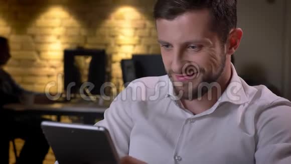 年轻开朗的白种人商人在平板电脑上打字在办公室里微笑的特写照片视频的预览图