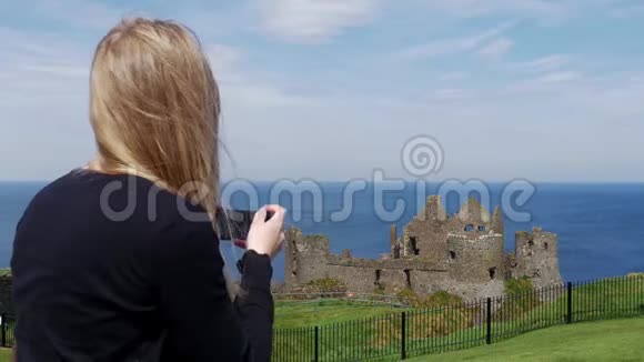 年轻女子在北爱尔兰拍摄邓卢斯城堡的照片视频的预览图