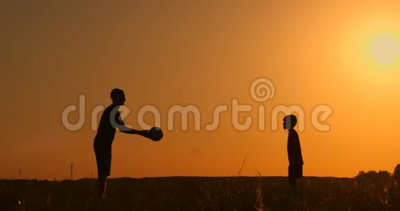 日落时分父亲和儿子在公园里踢足球在明亮的阳光下剪影动作缓慢视频的预览图