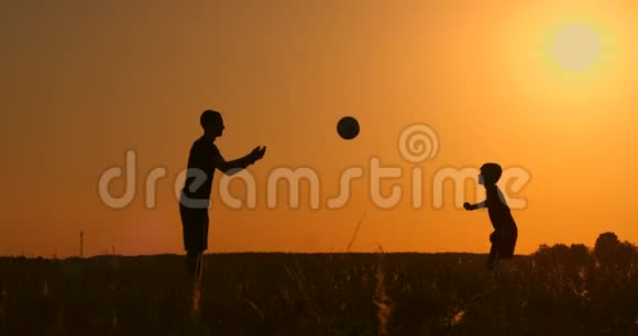 日落时分父亲和儿子在公园里踢足球在明亮的阳光下剪影动作缓慢视频的预览图