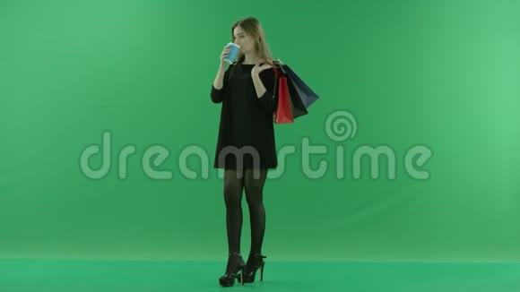 可爱的年轻女人在购物后喝鸡尾酒她的肩膀上有袋子颜色关键绿色背景视频的预览图