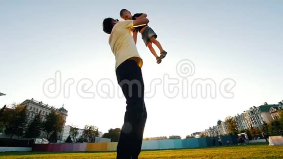 小伙子年轻的爸爸正抱着儿子在夏天的公园里空中旋转着他视频的预览图