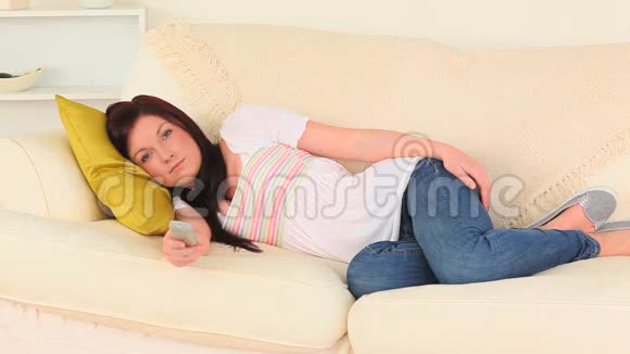 黑发女人躺在沙发上看电视视频的预览图