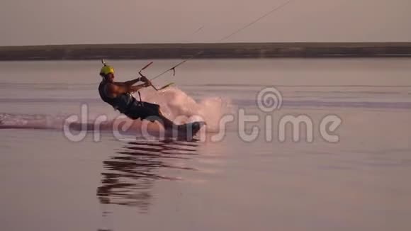 在粉红色的湖面上日落一个戴着头盔带着动作摄像机的人正在玩风筝视频的预览图