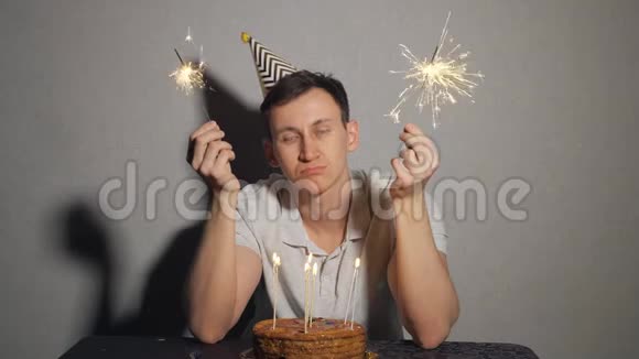 悲伤孤独的人戴着派对帽独自庆祝生日手里拿着火花视频的预览图