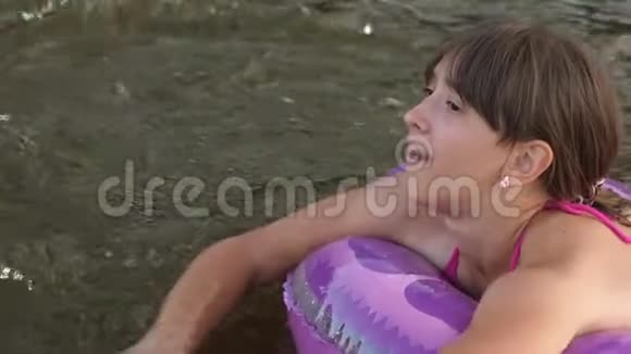 穿着泳装的瘦小女孩在救生圈的水面上漂下河笑了起来海滩季节视频的预览图