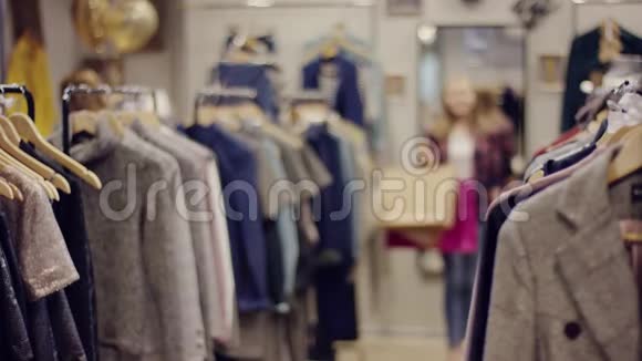 一位年轻漂亮的女士在一家服装店里走着手里拿着购物袋正在寻找一个新的衣服视频的预览图