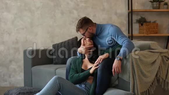 漂亮的年轻夫妇坐在现代阁楼内部客厅的沙发上接吻年轻漂亮的时髦女郎视频的预览图