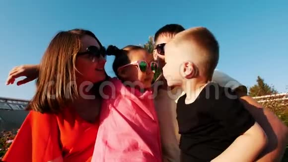 幸福的一家人坐在公园里的长凳上小儿子亲吻爸爸妈妈和姐姐视频的预览图