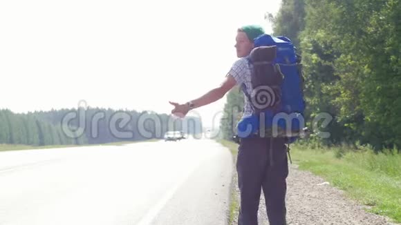 一个年轻人背着一个大背包从摄像机里按喇叭沿着路走视频的预览图