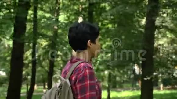 年轻开朗的女学生走着微笑绿色的公园背景快乐美丽的女人黑色的矮个子视频的预览图