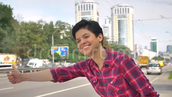 幸福的年轻女子一头黑发竖起大拇指寻找出租车站在城市道路附近的街道上视频的预览图
