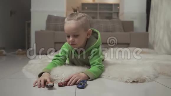 小男孩的肖像有时尚的发型在蓬松的地毯上躺在地板上玩玩具车视频的预览图