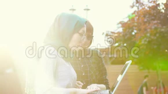 穆斯林学生戴着头巾她的朋友带着笔记本电脑高兴阳光明媚慢节奏视频的预览图