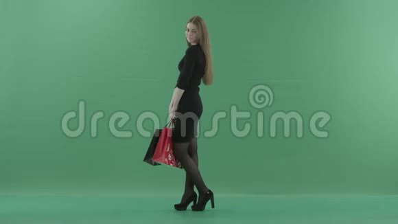 美丽快乐的女人穿着小黑裙子摆着购物袋她站在一间工作室里反对视频的预览图