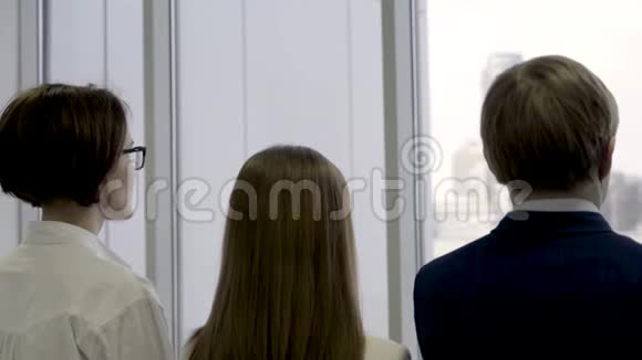 后视商务组站成一排透过窗户看两名女性和男性同事视频的预览图