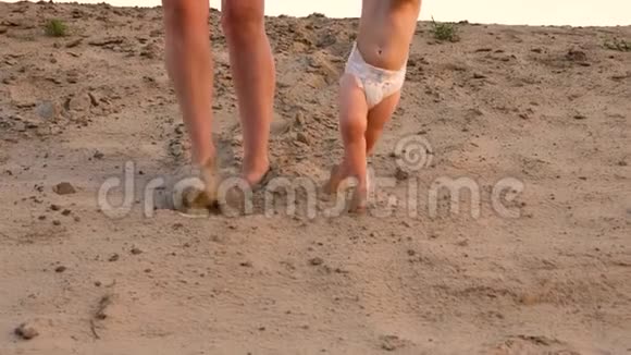 穿着尿布的小婴儿第一步走在沙滩上手牵着妈妈腿特写视频的预览图