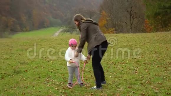 一位年轻的母亲和她的小女儿在秋天的森林里玩耍小美丽的女孩学会跳绳视频的预览图