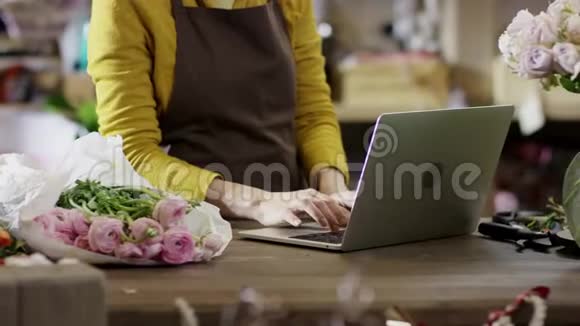 穿着黄色上衣的女人在花店工作在笔记本电脑上快速打印相机从下到上变化视频的预览图