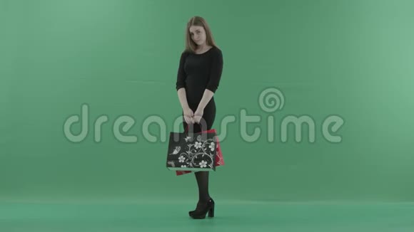 美丽的女人穿着黑色的小裙子摆着购物袋微笑着她站在演播室里反对视频的预览图