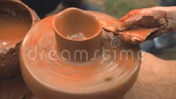 旋转陶工的车轮并在粘土器皿上做一个图案一个小孩用陶工的轮子上的泥杯雕刻他手视频的预览图