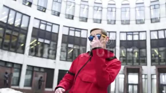 穿着红色运动服和太阳镜的帅哥在灰色的大建筑旁边跳舞视频的预览图