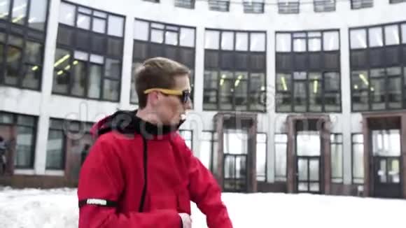 穿着红色运动服和太阳镜的可爱男人在灰色的大建筑旁边跳舞视频的预览图