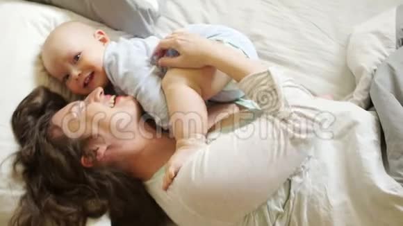女人挠痒痒拥抱她那岁的儿子阳光家庭早晨妈妈和宝宝在床上母亲节视频的预览图