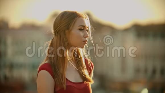 一位年轻有灵感的女士穿着红色的裙子站在明亮的夕阳下的屋顶上视频的预览图
