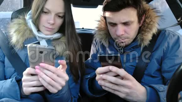 男人和女人坐在车里的手机里使用互联网视频的预览图