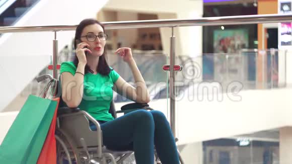 一位坐在轮椅上的残疾妇女购物后在购物中心的电话上聊天很有趣关门视频的预览图