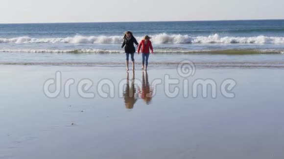在秋天寒冷的一天两个女孩沿着北爱尔兰的沙滩散步视频的预览图