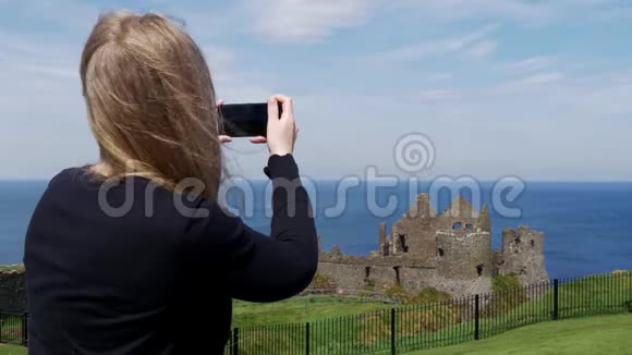 年轻女子在北爱尔兰拍摄邓卢斯城堡的照片视频的预览图