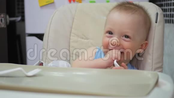婴儿坐在孩子们小桌子旁妈妈给孩子喂粥妈妈用勺子给婴儿食物视频的预览图