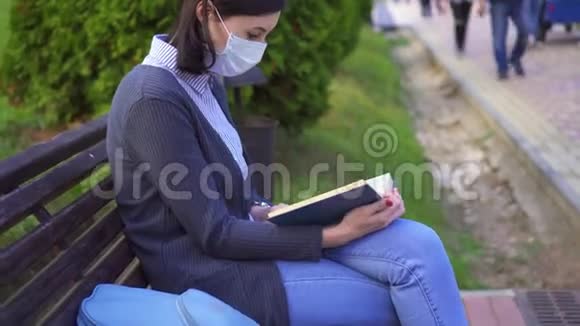 女孩坐在长凳上戴着一个保护性的医疗面具手里拿着一本书咳嗽起来视频的预览图