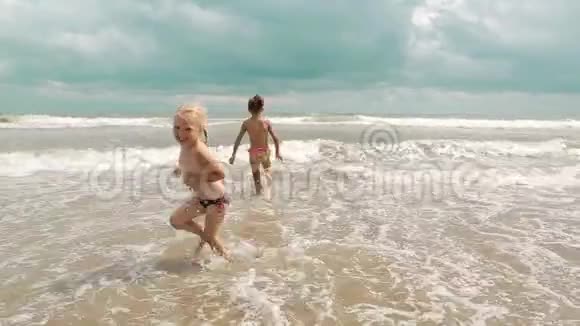 两个快乐的小女孩正在享受大海浪来岸边欢度小儿女视频的预览图