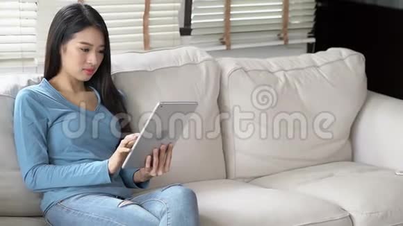 美丽的肖像亚洲年轻女士微笑着使用平板电脑快乐地坐在客厅的沙发上女孩在沙发上工作视频的预览图