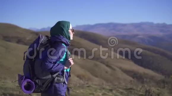 美丽的穆斯林女游客带着背包和太阳镜在美丽的山脉中旅行侧视视频的预览图