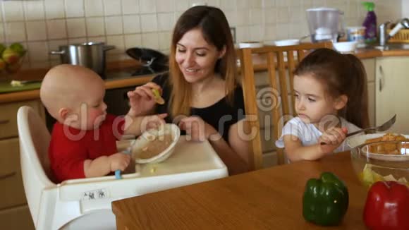 一家人在阳光明媚的白色厨房里吃早餐年轻的母亲喂养两个孩子儿童健康营养视频的预览图