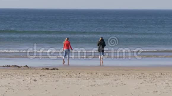在秋天寒冷的一天两个女孩沿着北爱尔兰的沙滩散步视频的预览图
