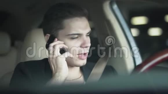 一个年轻人在汽车特写镜头中嚼口香糖和用手机说话的肖像视频的预览图