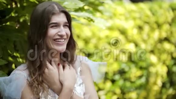 年轻漂亮的女人在绿色灌木丛的背景上摆着白色的裙子行动美丽精致的外表视频的预览图