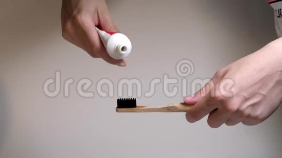 带有新鲜白色牙膏的牙刷黑色刚毛把牙膏从管子里挤到木制牙刷上视频的预览图