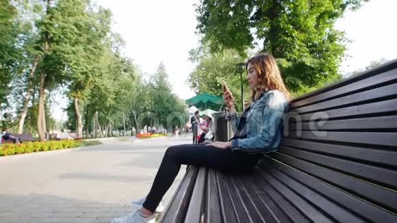 一个年轻的女孩坐在公园的长凳上脚附近是一个陀螺视频的预览图