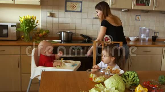 美丽的母亲在厨房里和她的两个孩子一个蹒跚学步的孩子和一个学龄前女孩母亲节视频的预览图