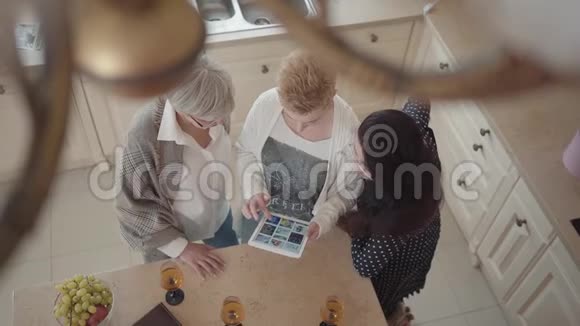 年长的女人在平板电脑上给她的朋友看照片三位中年成熟女性聊天小组视频的预览图