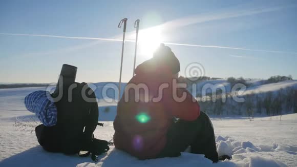 人类旅行者坐在冬天的山上的悬崖上喝热水瓶里的茶年轻人的后景视频的预览图