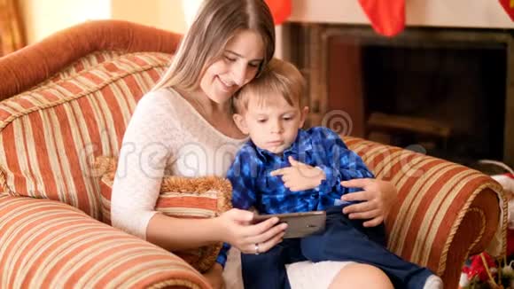 3岁可爱的幼儿男孩和妈妈坐在客厅的扶手椅上在手机屏幕上观看视频视频的预览图